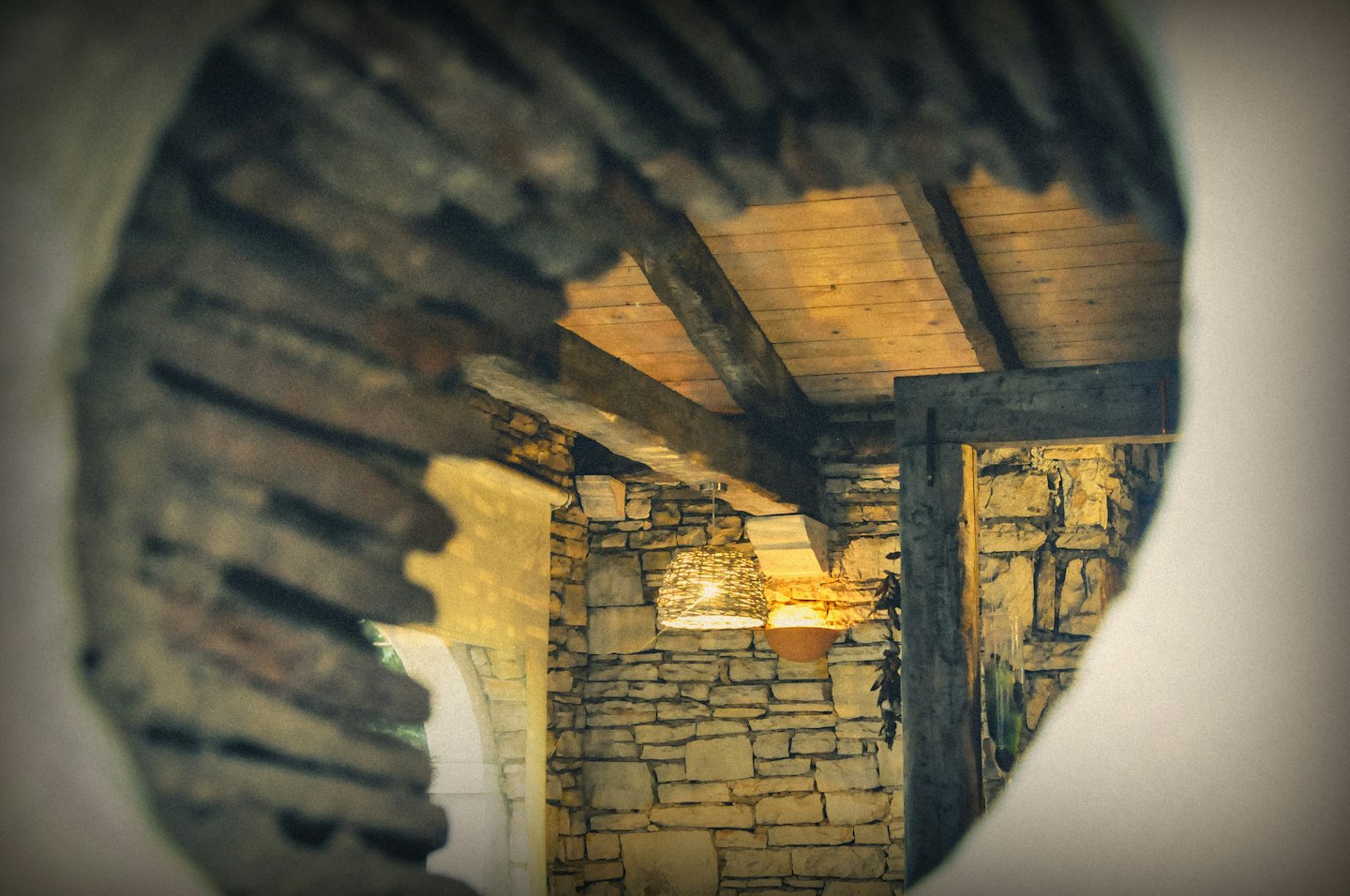 Una lampada a sospensione in vimini illumina pareti in pietra rustica e travi di legno.