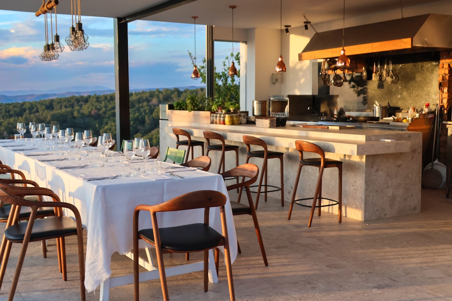 Un tavolo da pranzo apparecchiato si affaccia su un paesaggio montano da una cucina all'aperto.